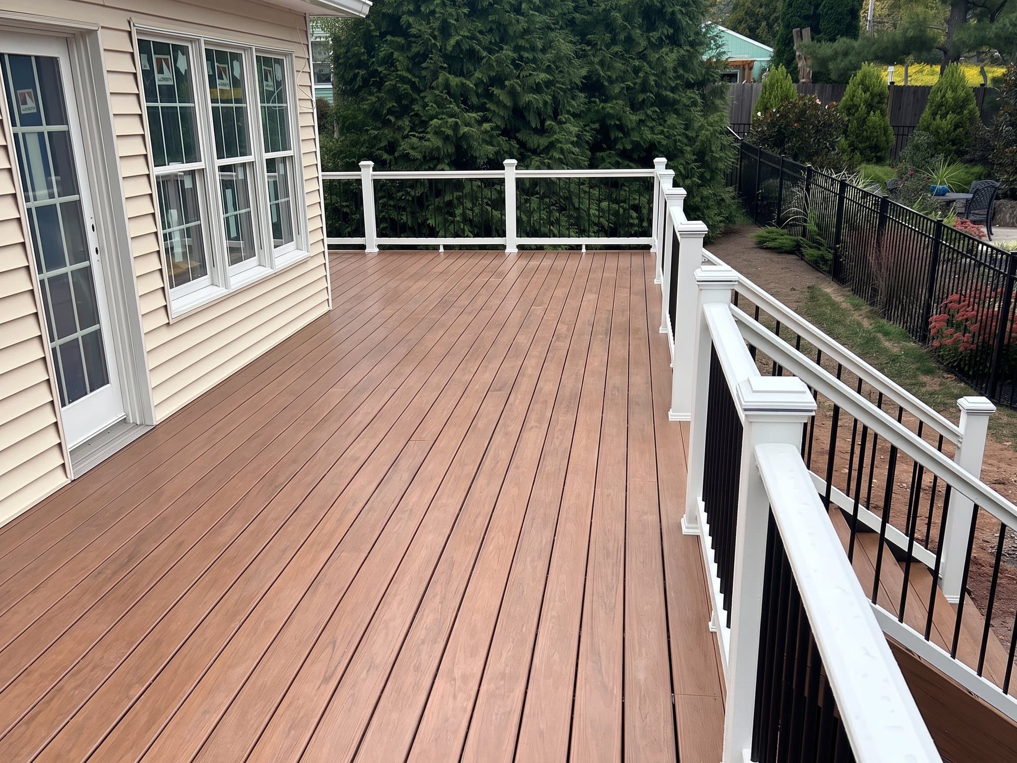 Long composite deck along the back of a house with white railing and black balusters