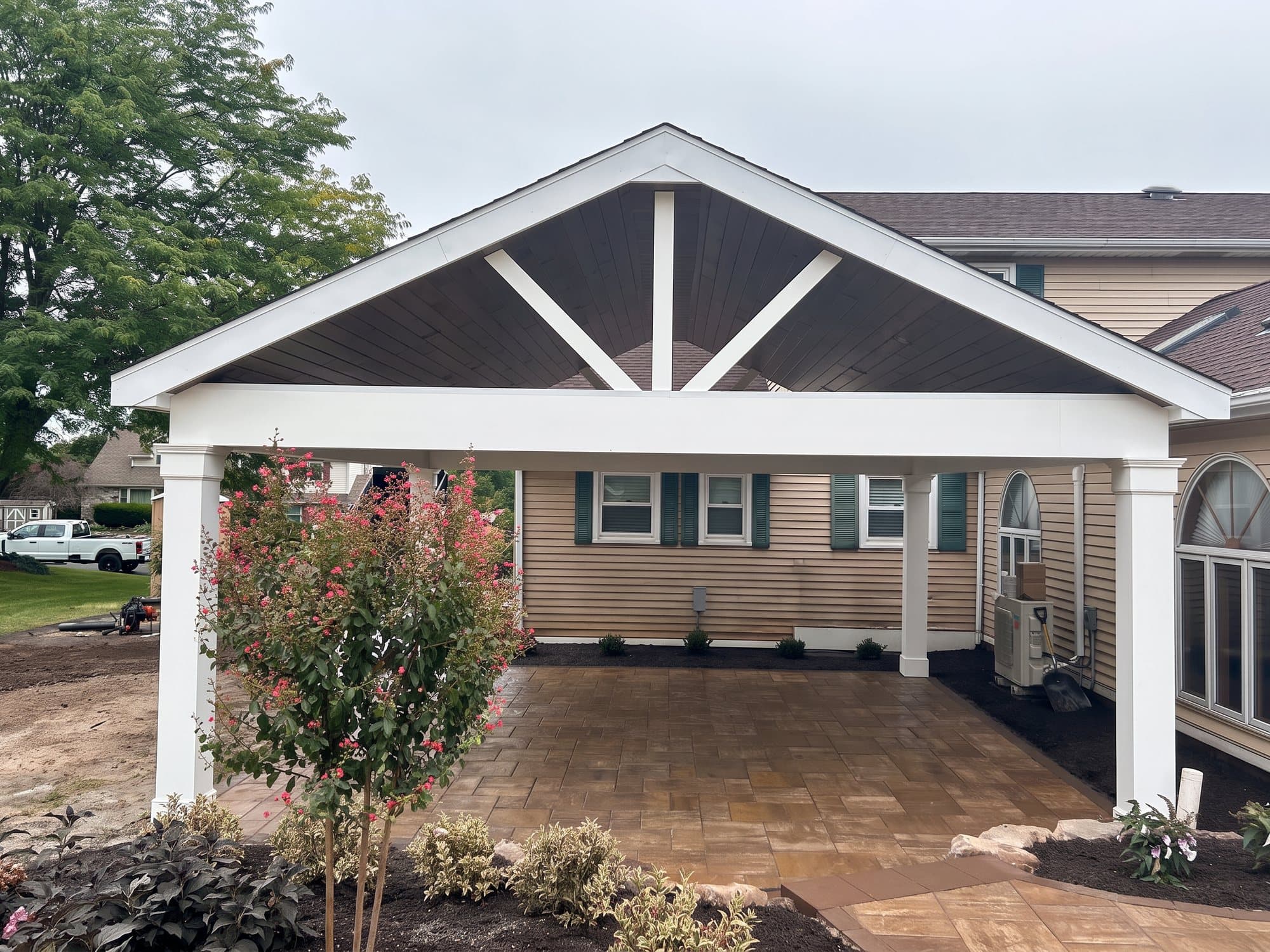 White gable-roof pavilion with a stained ceiling over a paver patio, with new landscaping