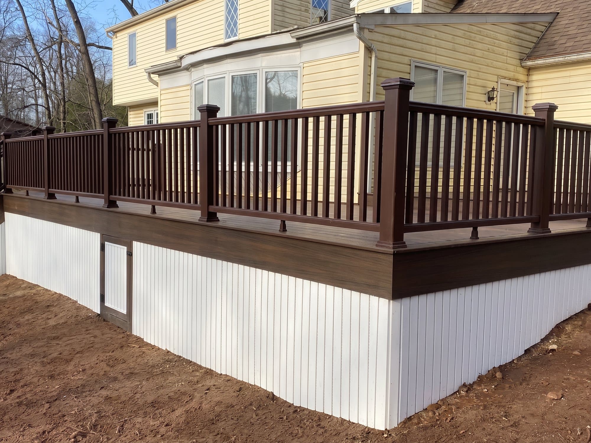 Raised composite deck with brown railing and white vertical skirting with an access door