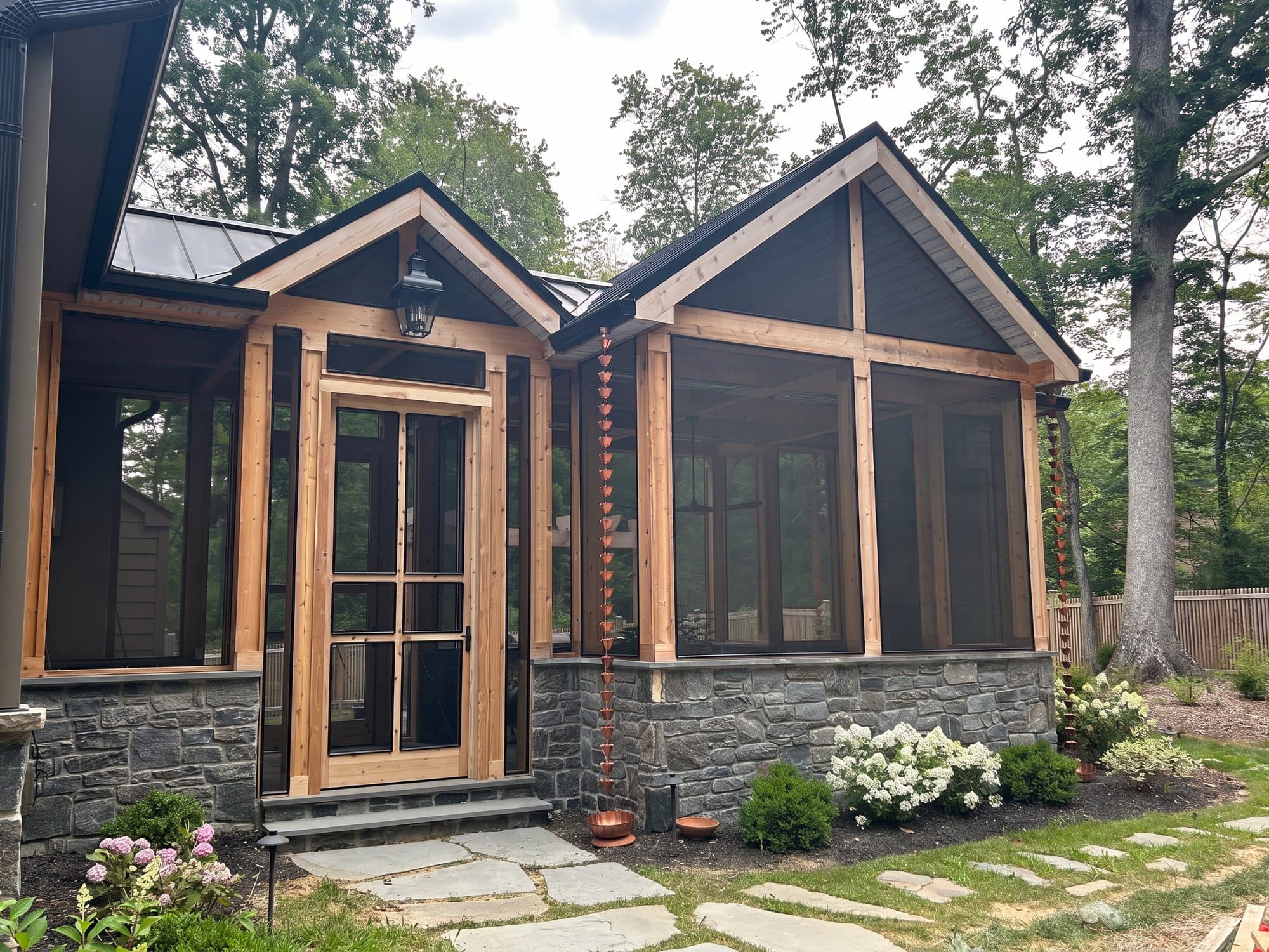 Screened porch with timber framing, gable roofs, stone knee walls, and copper rain chains
