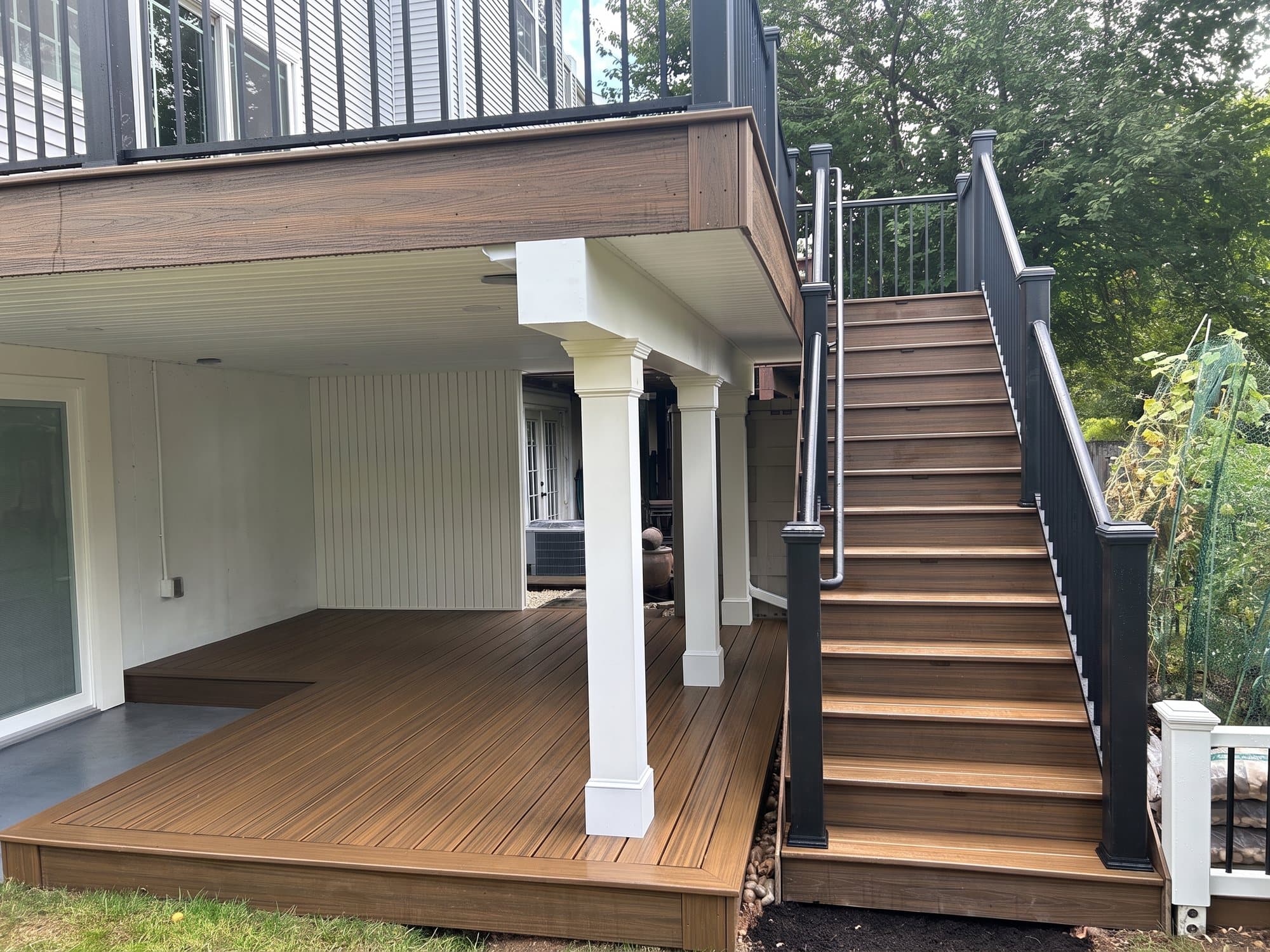 Upper deck with black railing above a covered lower deck with white columns and a long staircase